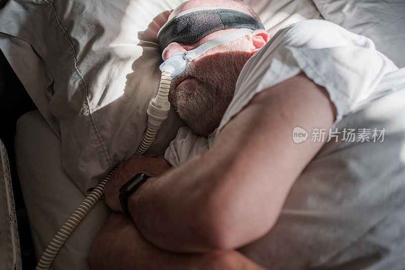 成年男子在被诊断为睡眠呼吸暂停并戴着睡眠面罩后，用CPAP(持续气道正压通气)机睡觉