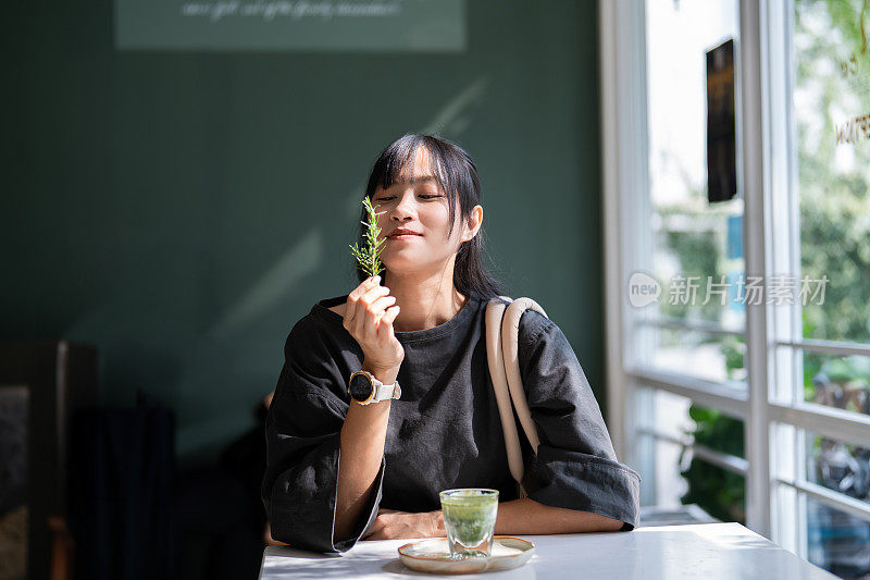 亚洲女性在现代咖啡馆品尝热腾腾的抹茶绿茶，呼吸迷迭香。