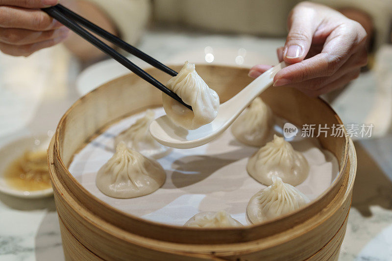 用筷子夹着小笼包的女性手特写，这是一种放在竹制蒸笼里的中国传统食物。