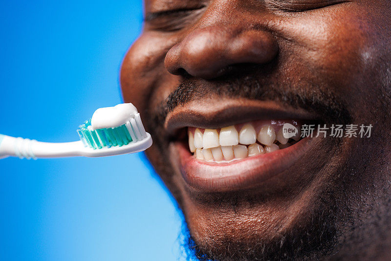一名黑人男子拿着牙刷摆姿势，宣传定期刷牙对健康微笑的重要性