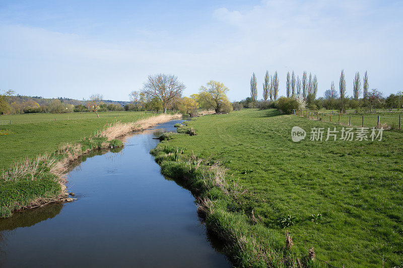 巴伐利亚的风景照片。一条小溪穿过一片绿色的草地。在地平线上可以看到一棵棵树。现在还在年初。