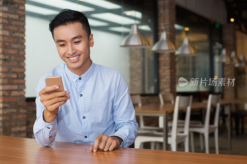 微笑的亚洲男人在咖啡桌上使用智能手机