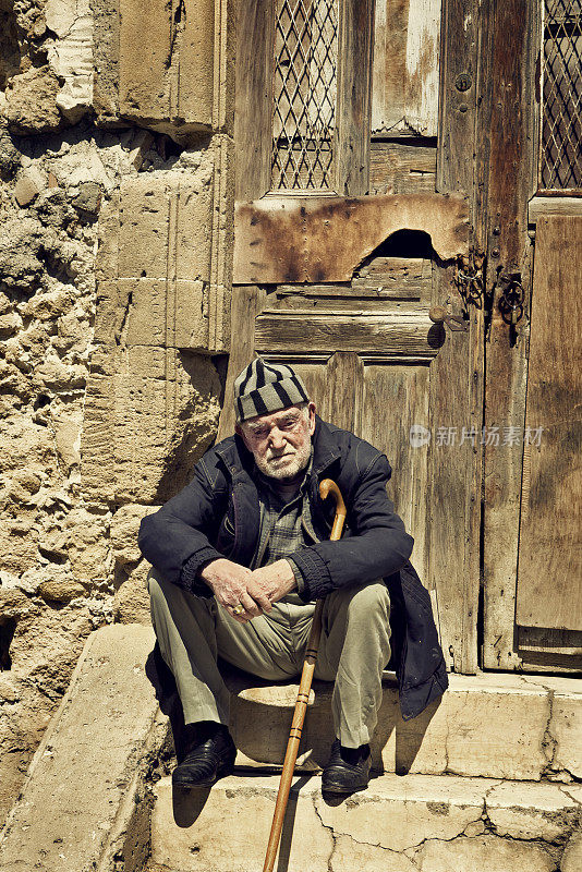 一个老人坐在一间废弃房子的门槛上