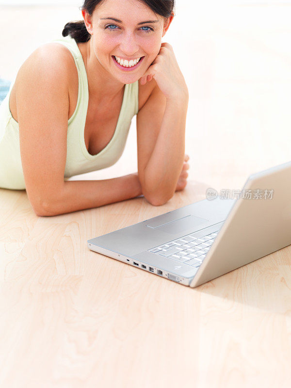 一个快乐的年轻女人躺在地上，前面放着笔记本电脑