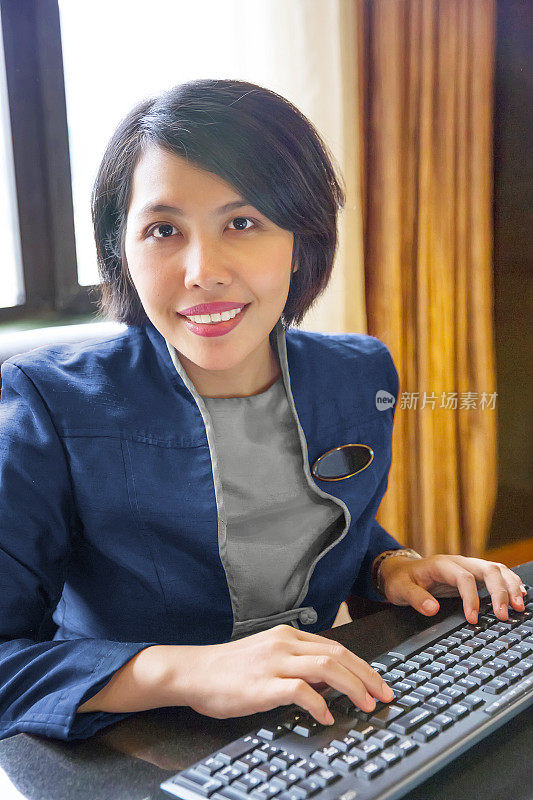 亚洲女性酒店礼宾坐在电脑键盘前