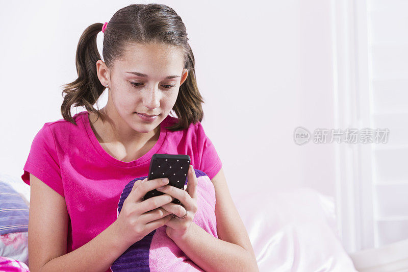 穿着睡衣坐在床上发短信的女孩