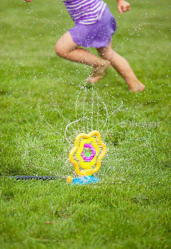 女孩跑过洒水器在草地上