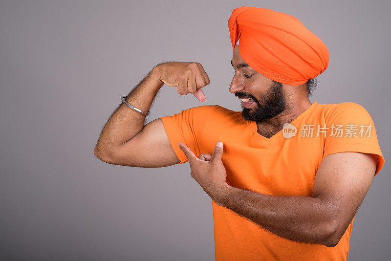 在灰色背景下，年轻的印度锡克教男子穿着橙色衬衫和橙色头巾