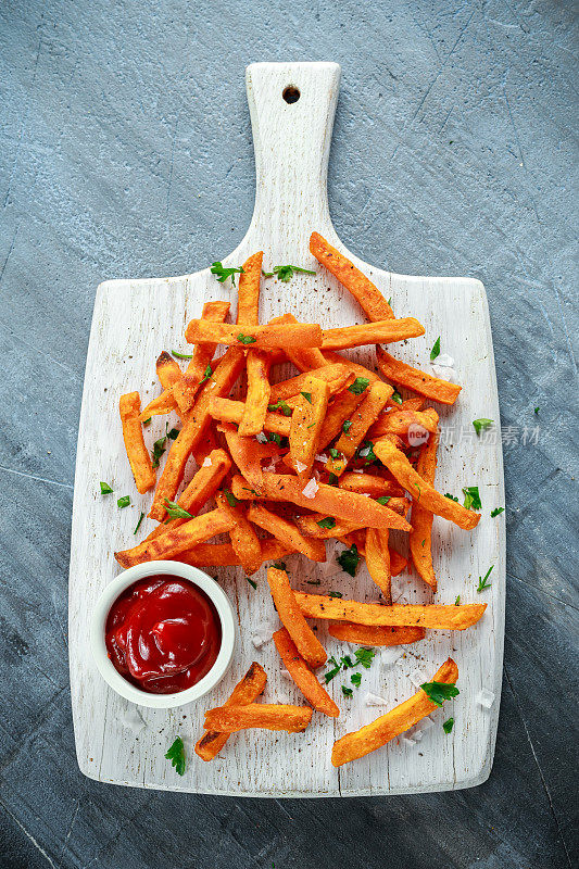 健康自制烤橙甘薯薯条配番茄酱，盐，胡椒在白色木板上