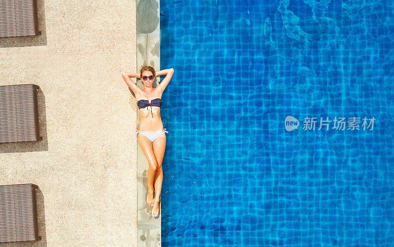年轻女孩在比基尼和太阳眼镜晒太阳接近游泳池，俯视图