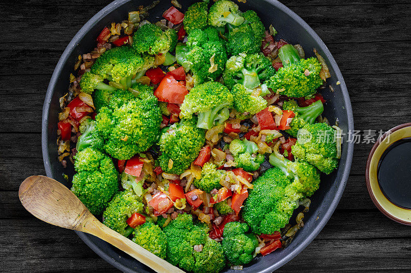 新鲜的夏季沙拉。清炒蔬菜、西兰花、酱油、伊比利亚火腿丁放在质朴的木桌上。健康食品的概念。