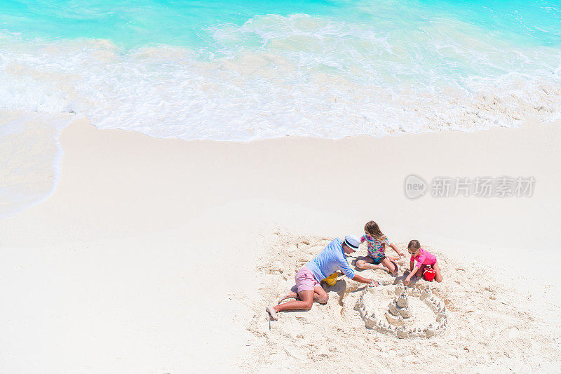 父亲和小女儿们在热带海滩上建造沙堡