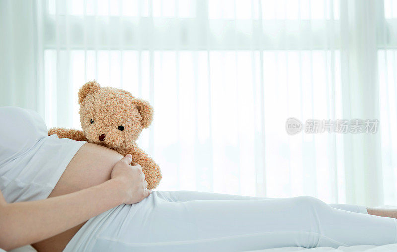 一个孕妇抱着一只泰迪熊躺在床上