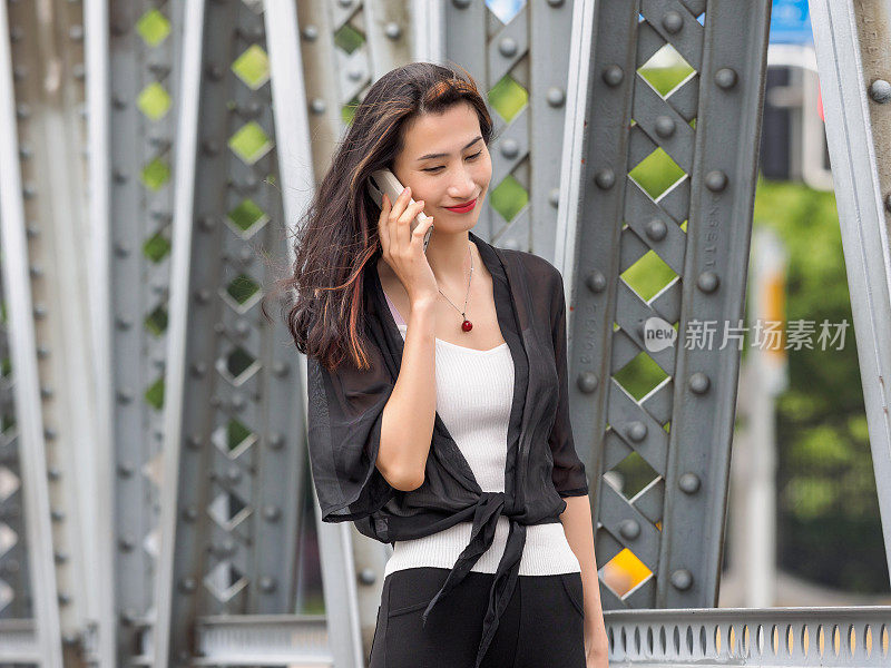 快乐的成年亚洲女人的电话，与上海花园桥的背景。