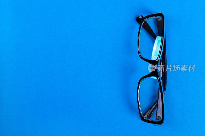蓝色背景的现代时尚办公眼镜，完美的反光，桌子上的眼镜用于复印空间