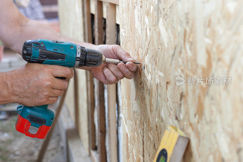 建筑工人用螺丝刀将木屑板(纤维板)固定在墙上