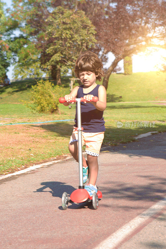 快乐的小男孩骑着他的摩托车在当地的公园里。可爱的学前班小男孩在公园里骑滑板车。