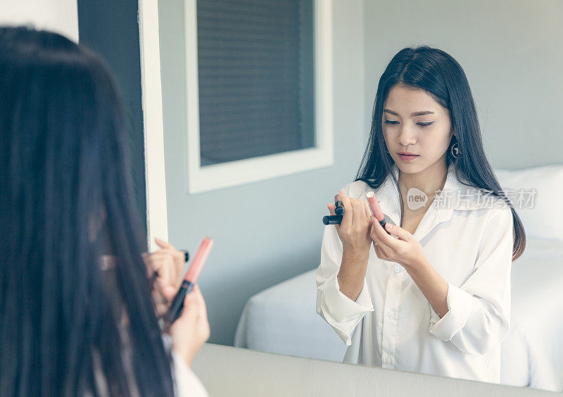 年轻漂亮的女人穿好衣服，在镜子前用口红化妆