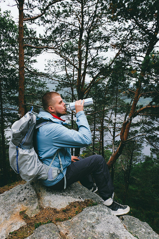 背着背包的男子在挪威的布道石徒步旅行时喝水