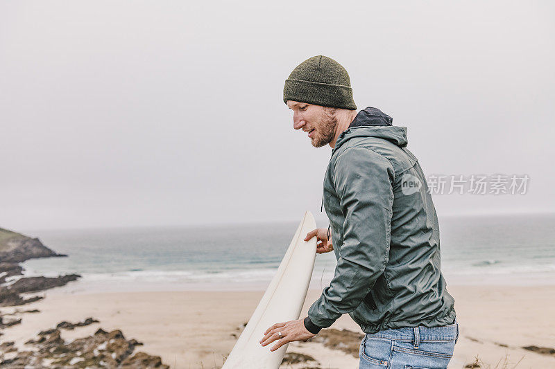秋天的一天，康沃尔纽基菲斯特拉海滩上，一个男人带着他的冲浪板。