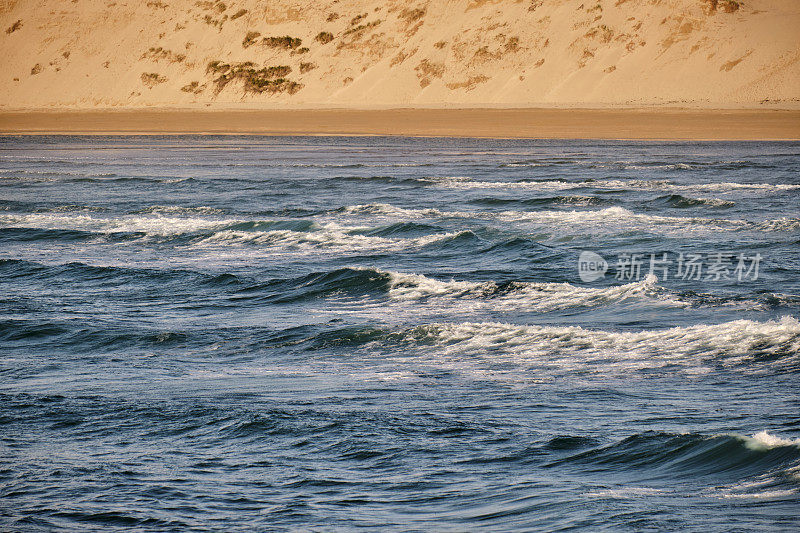 在一个明亮的夏天晚上，透过海浪看到克兰托克海滩的沙丘。