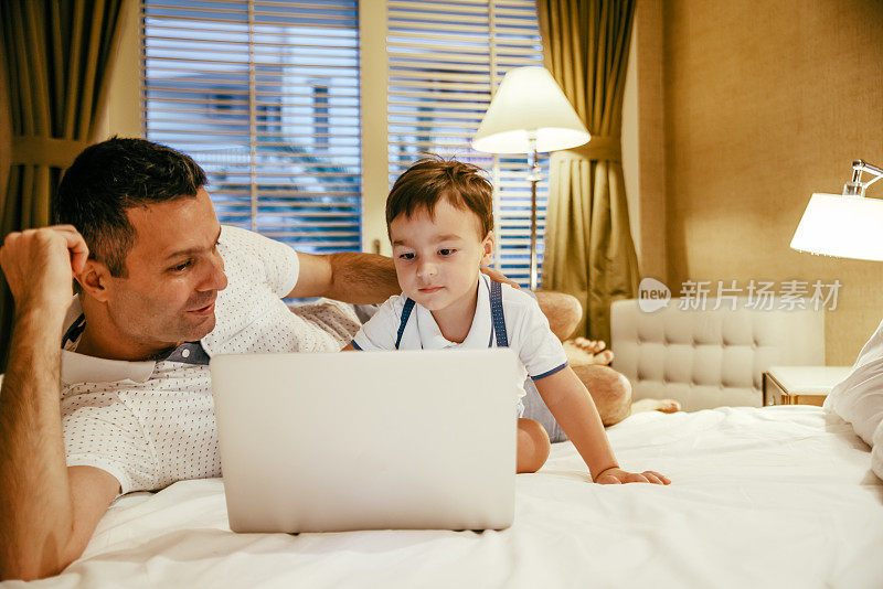 父亲和儿子在床上玩笔记本电脑