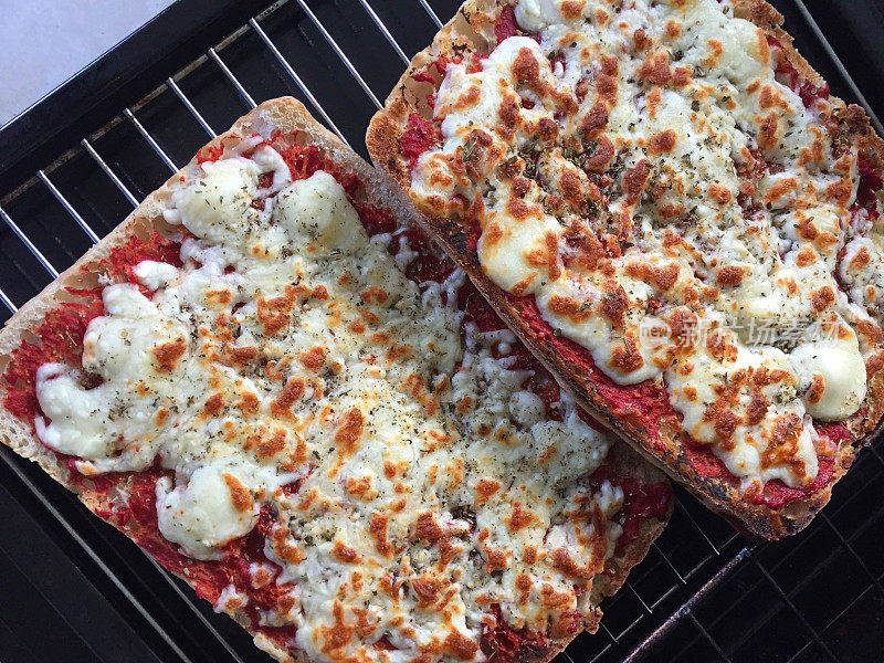 这是切片的查巴塔面包作为披萨风格的底座放在金属烤炉上的特写，上面覆盖着番茄酱和融化的马苏里拉奶酪