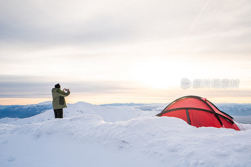 年长的高山攀登者正在冬季高海拔的山峰上用手机拍照