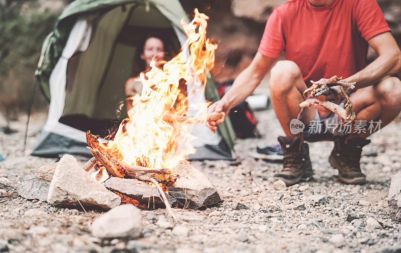 幸福的夫妇在野外露营时生火-年轻人有乐趣的旅行和露营下篝火-旅游度假的生活方式概念