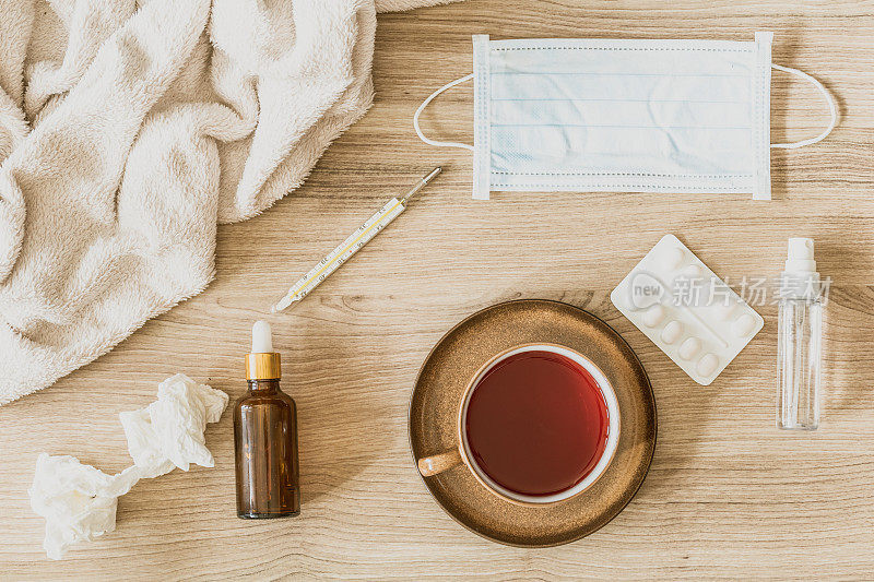 冠状流感病毒检疫的概念-抗菌洗手液，胶囊和药丸，医用口罩，茶杯茶，温度计，纸巾，毯子和口服滴在木制背景