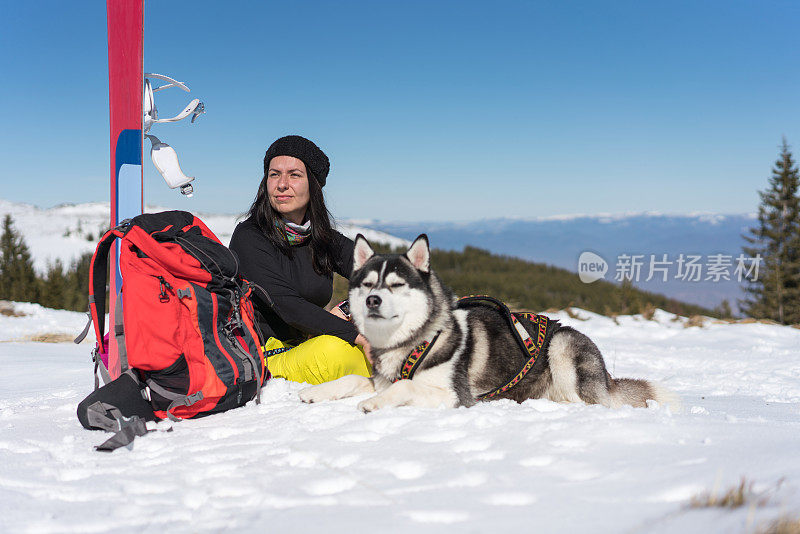 女滑雪者与她的西伯利亚哈士奇在雪地上放松