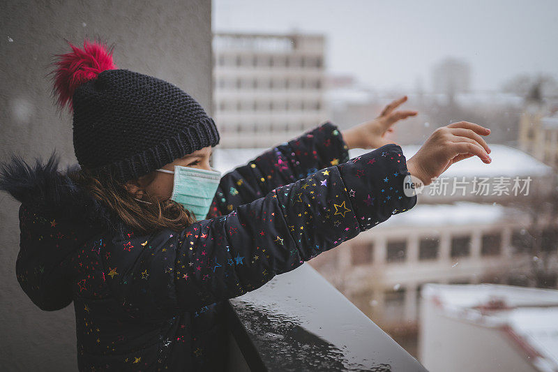 在自我隔离期间，可爱的小女孩试图从阳台上捕捉雪花