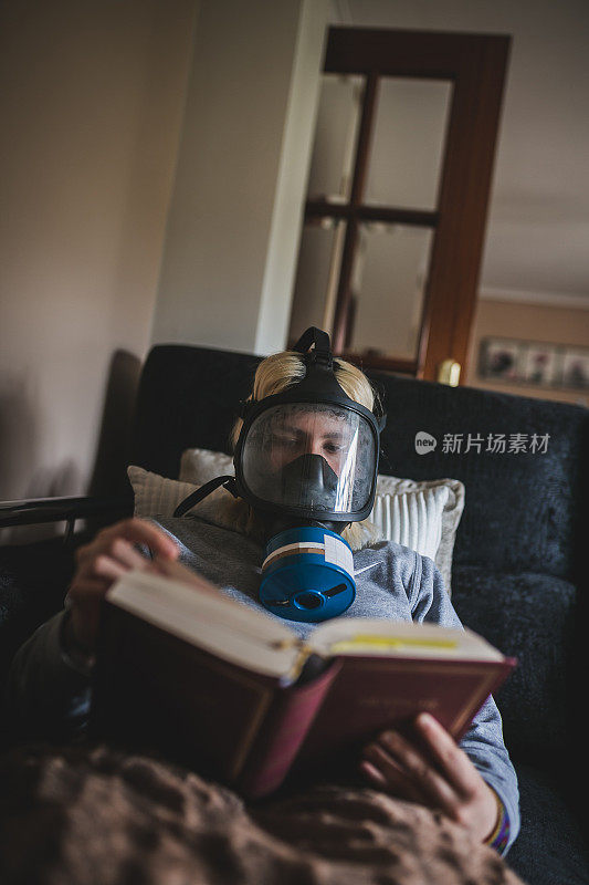 年轻女子戴着面具在家看书。