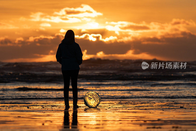 日出时，女人在海滩边拿着水晶球