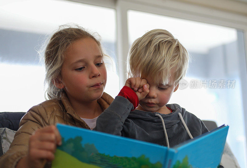 一个小女孩给一个小男孩读故事书。