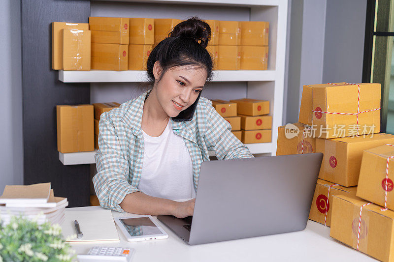 女人通过智能手机和电脑笔记本电脑在家庭办公室在线销售产品