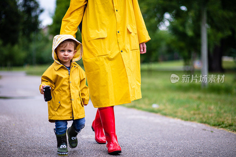 母亲和蹒跚学步的孩子，男孩，在雨中玩耍，穿着靴子和雨衣