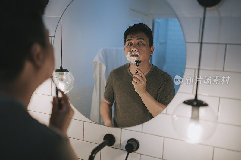 亚洲华人男子在盥洗室对着镜子刮胡子