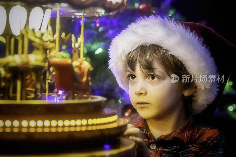 小男孩戴着圣诞老人的帽子看着玩具旋转木马
