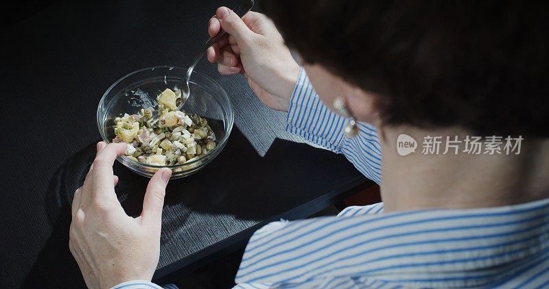 越过肩膀，一个成熟的女人坐在桌子上吃土豆沙拉