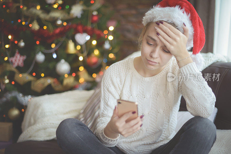 年轻女子在圣诞节室内与智能手机(网上约会)