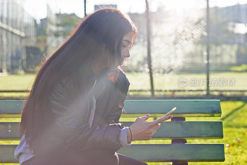 一名年轻女子坐在公园的长椅上玩手机