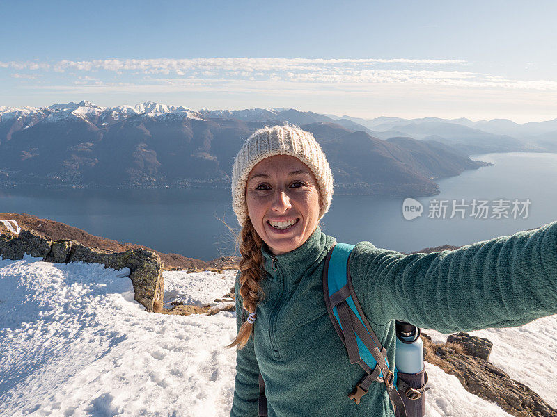 女徒步旅行者在山顶自拍。活跃的有吸引力的女人在徒步旅行与山脉和湖泊在远处的酷自拍