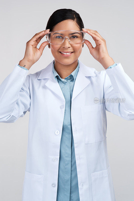 一位迷人的年轻女科学家的裁剪肖像戴着护目镜在工作室的灰色背景