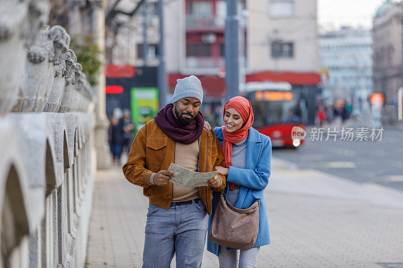 年轻的非洲男子和他的穆斯林妻子带着旅游地图在市区散步。