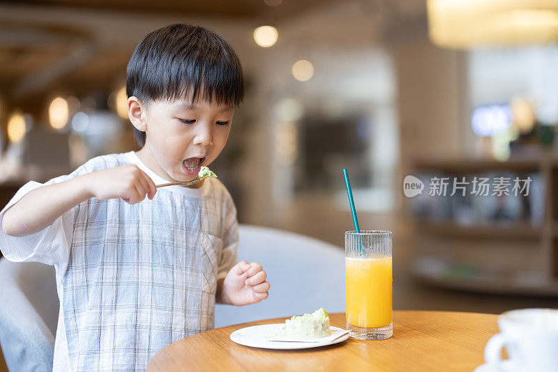 这个小男孩正在喝果汁，吃甜点