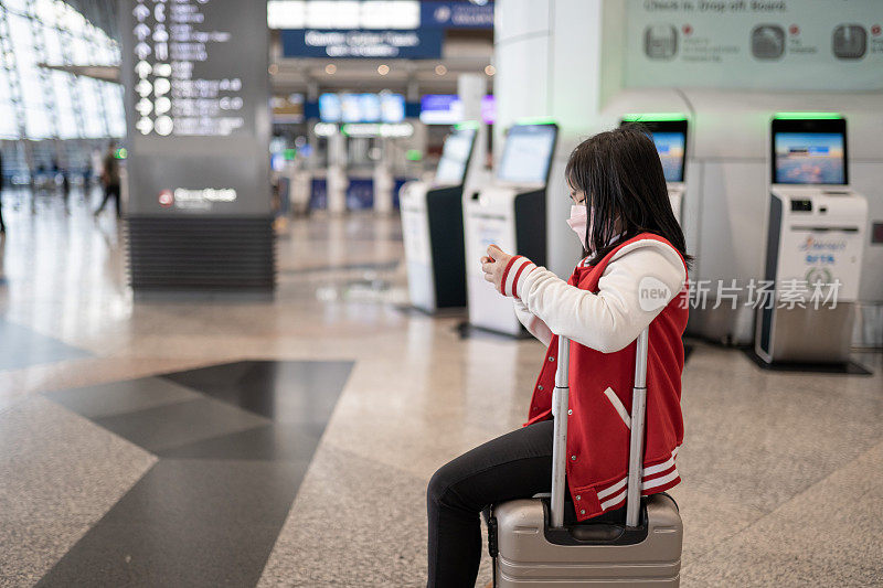 亚裔中国女孩戴着口罩，用智能手机上网，在机场候机。