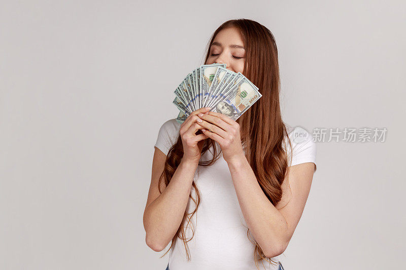 黑头发的女人闻着美元钞票，享受着彩票中奖，丰厚的利润和富裕的生活。