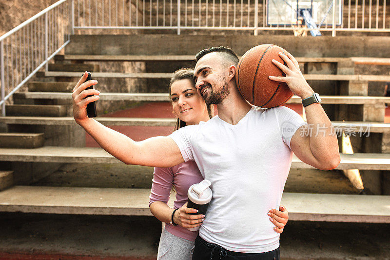 年轻情侣在街头球场打篮球时自拍