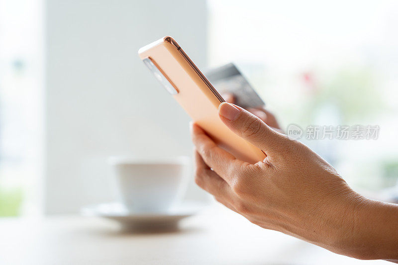 亚洲女性在一家舒适的咖啡馆用智能手机网购，用信用卡进行移动支付